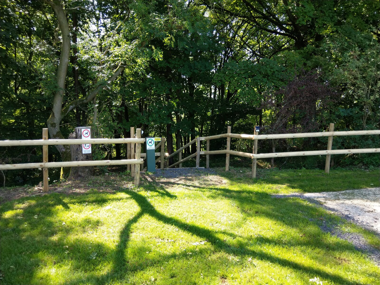 A post-and-rail fence and gated woodland path with dog-walking signs