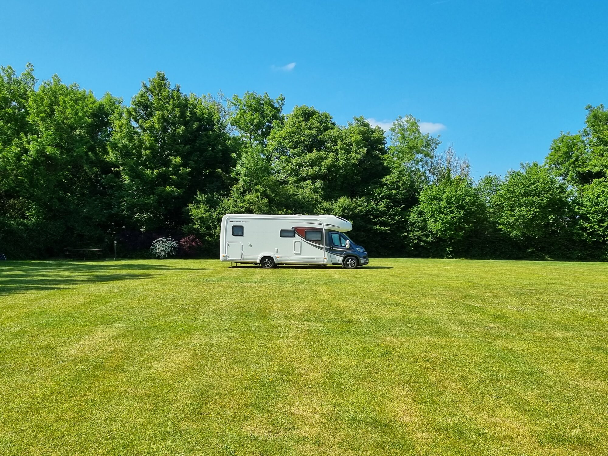 A motorhome pitched on the sunny open grass field at Woodside Field under a clear blue sky