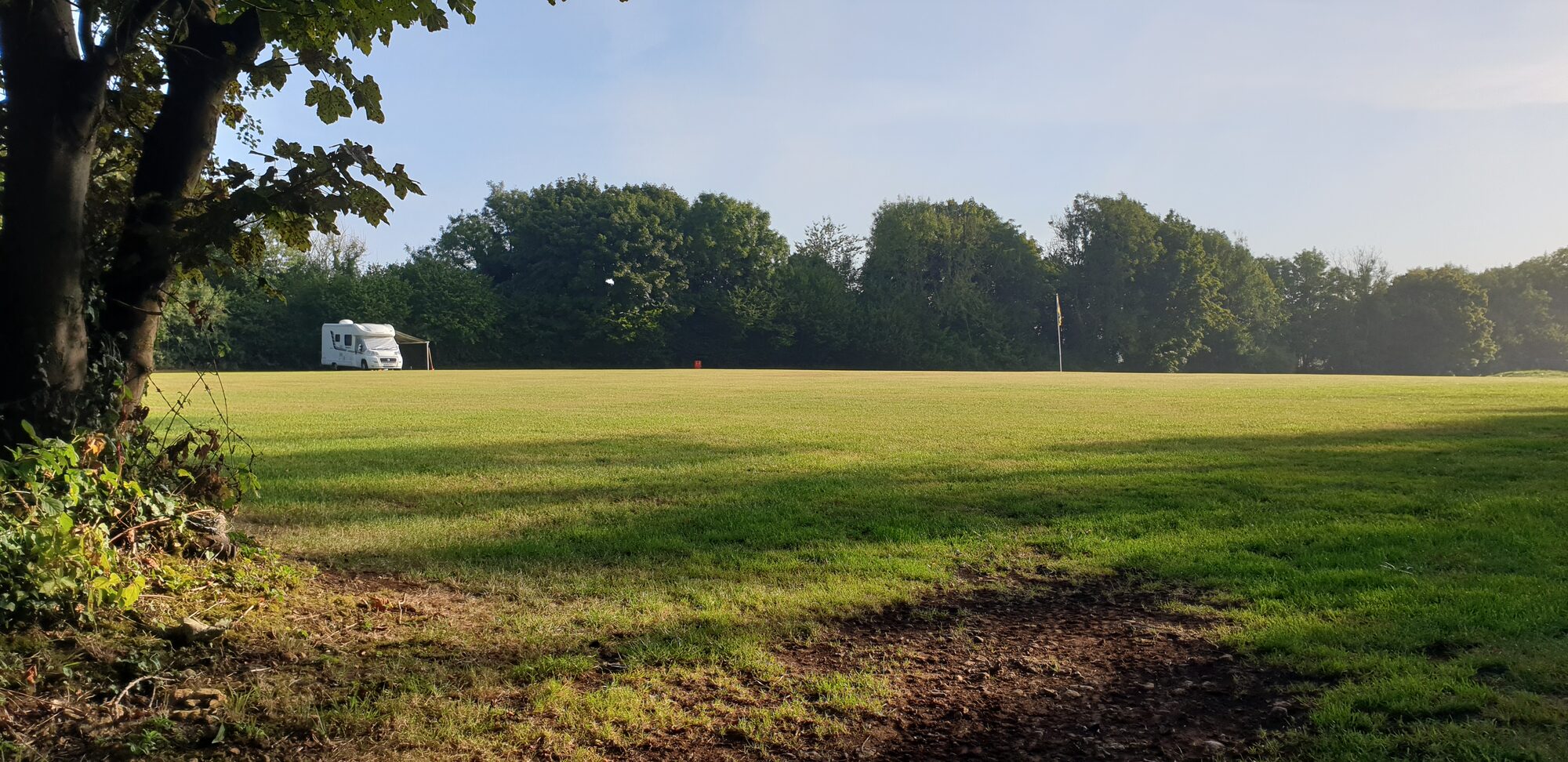 Morning sun on the open field at Woodside Field, with a motorhome pitched beside the trees