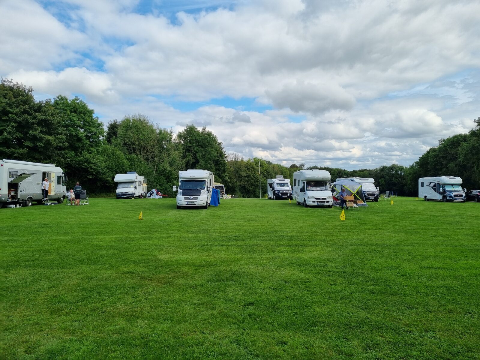 A line of motorhomes pitched along the hedgerow during a rally under blue skies