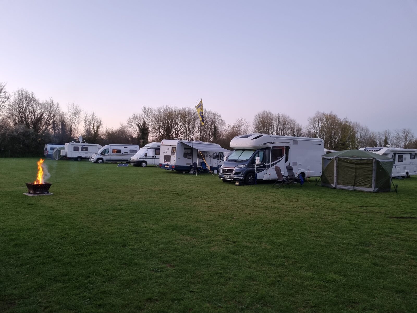 Motorhomes gathered on the field at dusk with a campfire burning